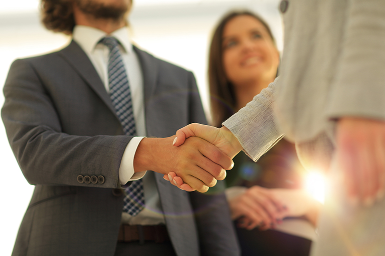 Businesspeople  shaking hands against room with large window loo